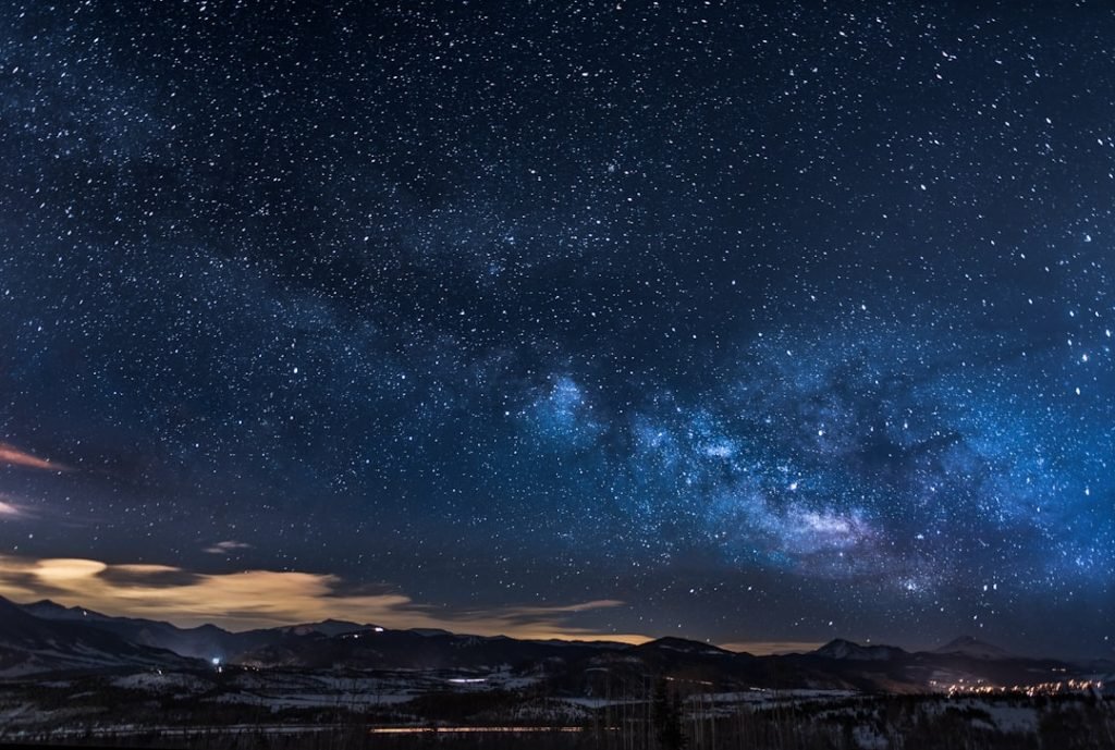 A clear night sky filled with stars and a faint zodiac wheel overlay, evoking astrology and celestial themes